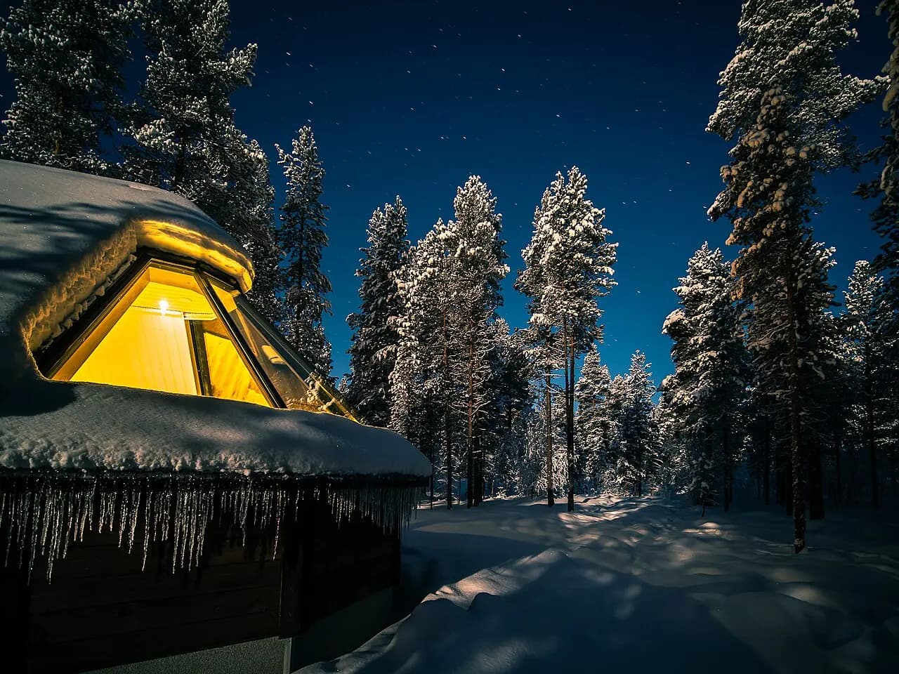 A glass-roofed aurora cabin at Aurora Village Ivalo in deep snow at dusk